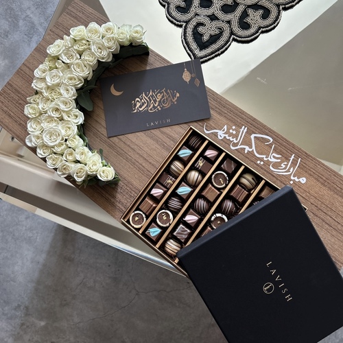 Lavish Flowers - Neqsa Helal Ramada II - contains a small crescent-shaped rose, a 500-gram box of chocolates, and a greeting card.