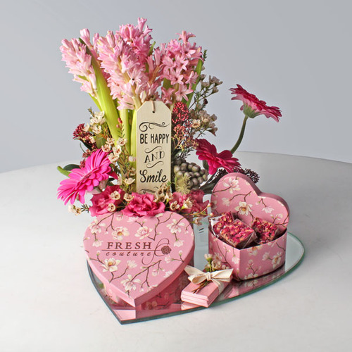 Mon Amoure 27 - 2 heart shape pink box contains chocolates on a heart shape mirror tray decorated with gergera, hysinthus, wax flowers, bromea and skimmia flowers with quoted wood.