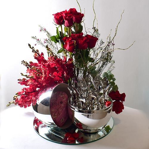 You & Me 40 - stainless
  utensils with egg shape holder decorated with fresh orchis and roses flowers
  with heart box of chocolates on a mirror tray.