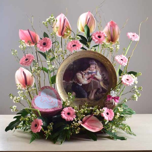 janati 5 - Gold
  painted decorative plate display with a decoration of fresh gerbera, wax
  flowers and anthorium flowers with 1 heart box of chocolates inside.