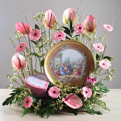 janati 6 - Gold
  painted decorative plate display with a decoration of fresh gerbera, wax
  flowers and anthorium flowers with 1 heart box of chocolates inside.