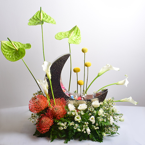 Helal Gergean 12 - A
  vase in the shape of a crescent moon contains Ramadan sweets, chocolate and
  gergean decorated with natural flowers, anthurium, calla, pines, lisiantus
  and wax flower