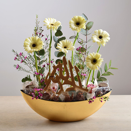 eid adhha & haj mabror 12 - tray
  with arabic writing stand with chocolates and a decoration of fresh gerbera
  and wax flowers.