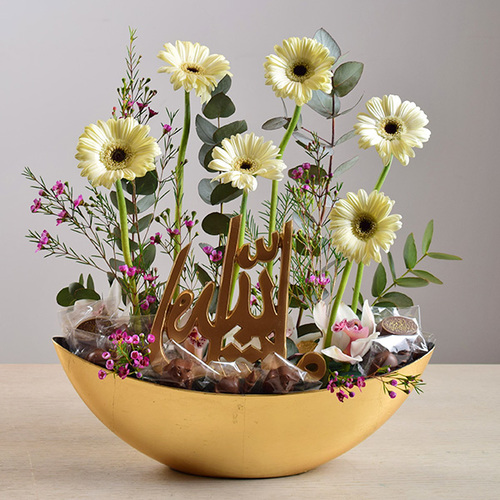 eid adhha & haj mabror 13 - tray
  with arabic writing stand with chocolates and a decoration of fresh gerbera
  and wax flowers.