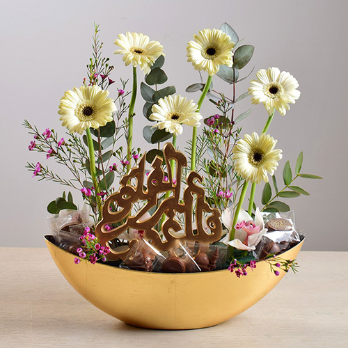 eid adhha & haj mabror 14 - tray
  with arabic writing stand with chocolates and a decoration of fresh gerbera
  and wax flowers.