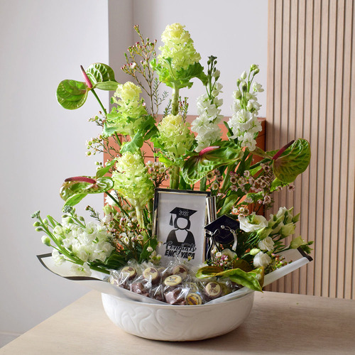 Graduation Gift - Graduation
  Can tray with picture frame, chocolates and a decoration of fresh brassica,
  anthorium matola, and wax flowers.