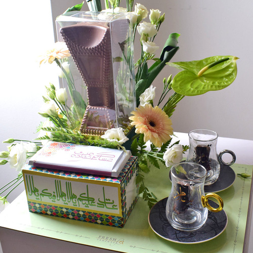 Me & You 10 - Mubhkar
  Chocolate with box of kuwaiti sweets, chocolate Bar and 2 ceramic tea cups
  set with plates and a decoration of fresh gerbera, anthorium and lisianthus
  flowers on a board tray.