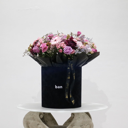 Purple Reign - A collections of flowers with the shades of pink and purple. A bouquet of roses, chrysanthemums, gerbera, lisianthus with greens inside a black velvet cylinder. H 55 x W 55 cm.