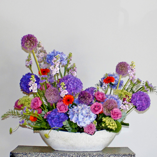 Luxurious Purple Boat - An oval boat shape vase of purple shades flowers hydrangeas, allium, matthiola, roses and orange gerbera flowers. H 80 x W 90