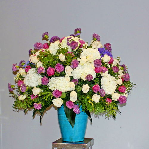 Amore - A big flower arrangement that contains white and purple hydrangeas, roses and carnations with greens in a blue vase.