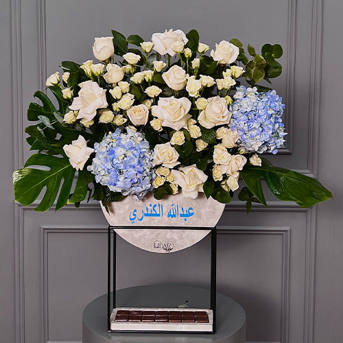 Baby Blue - High vase contains blue hydrangea, white rose, white baby rose, greens and Belgian chocolate. Optional: writing on the item maximum 18 characters. Hight 86  Width 85