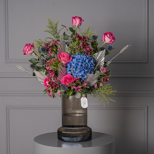 Evelyn - Glass black vase contain blue Hydrangea, pink rose, pink alstroemeria, green solidago, silver palm spear and silver triticum. Height 77 Width 56