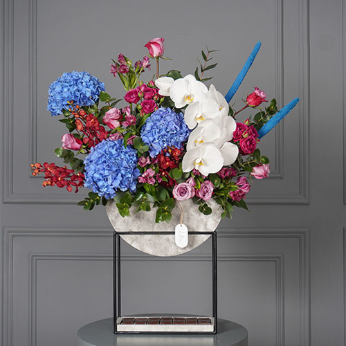 Leo - Stand contain blue Hydrangea, white Orchid, red baby Orchid, purple Roses and Belgian chocolate. 
 Height 90  Width 75