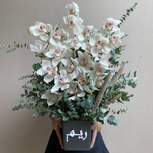 Pure White - White cymbediums arranged in a customized grey leather vase *Write the desired name in the message box*Flower kind and color may slightly
differ based on availability.