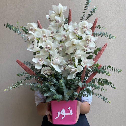 Dreamy White - White cymbediums arranged in a customized pink leather vase *Write the desired name in the message box*Flower kind and color may slightly
differ based on availability.