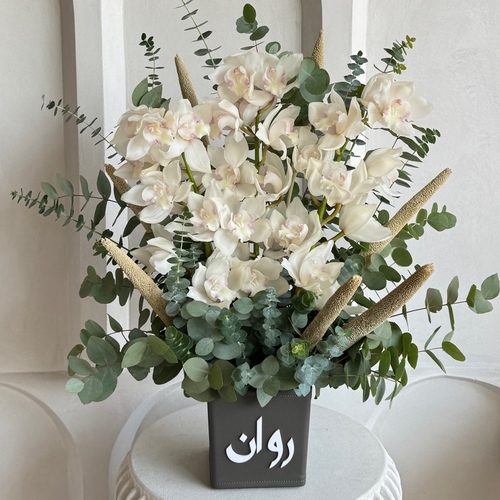 Fleurette - Pure White - White cymbediums arranged in a customized grey leather vase *Write the desired name in the message box*Flower kind and color may slightly
differ based on availability.