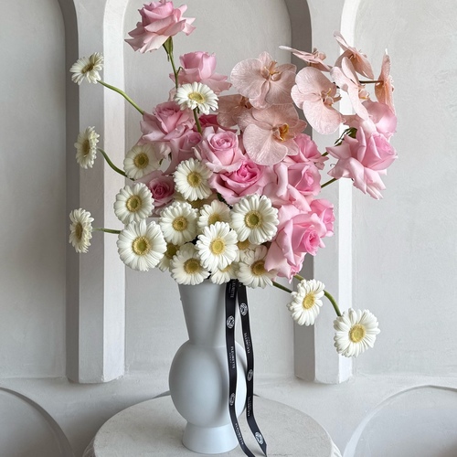 Blooming bliss - An arrangement of roses, gerbera, and orchid in a tall white vase. *Color and kind of flowers may slightly differ based on availability