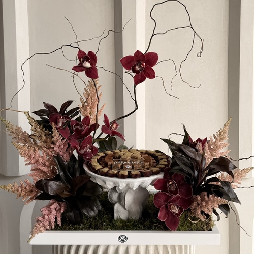 Neqsat Alsafaa - A decorative white ceramic stand in a big white tray decorated with flowers and rangina with pistachio, cinnamon and caramel with ramadan phrase *Flower colors and kind may slightly differ based on availability