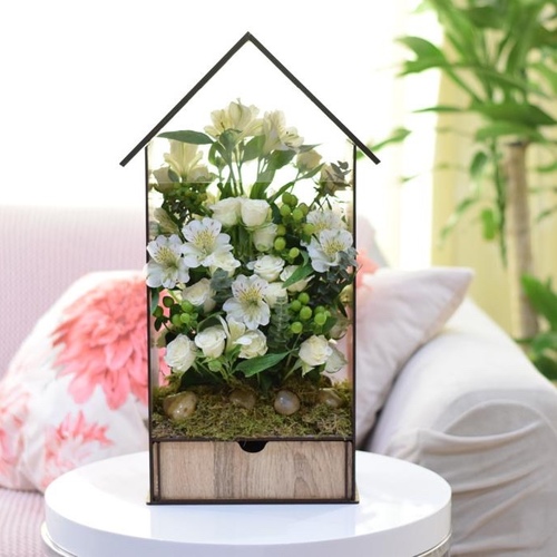 White House - A beautiful house containing baby rose flowers, astomaria, grass, and green plants, in addition to 20 luxurious pieces of chocolates