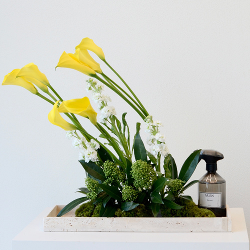 Sunrise - A travertine tray that contains calla lily and delphinium flowers with a home spray.