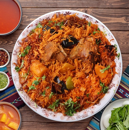 Meat Red Kabsa - Basmati bread cooked in meat broth, cooked in the Kuwaiti way, with a piece of fresh meat added to it, served with potato broth or daqoos, two types of maabouj, and a box of onions and watercress.