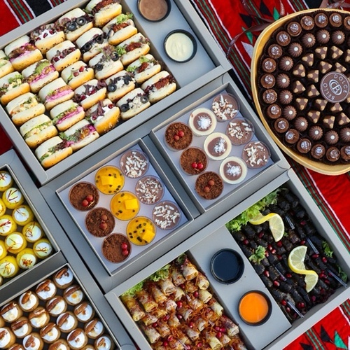 Mokhayam Offers - - A tray of 70 Belgian chocolates with three different fillings
- A box of 18 delicious mousse cups in four different flavors: chocolate, coconut, tropical fruits, and tiramisu
- A mixed box of 25 saffron-flavored Aqili cookies and 25 date-pecan cookies, totaling 50 pieces for the box
- A large box of 25 mini sandwiches with five different fillings: chicken chutney, labneh with buttermilk, Kraft cheese, halloumi, and olive cream cheese
- A box of 80 stuffed grape leaves and musakhan (40 musakhan and 40 stuffed grape leaves), plus French sauce and pomegranate molasses sauce