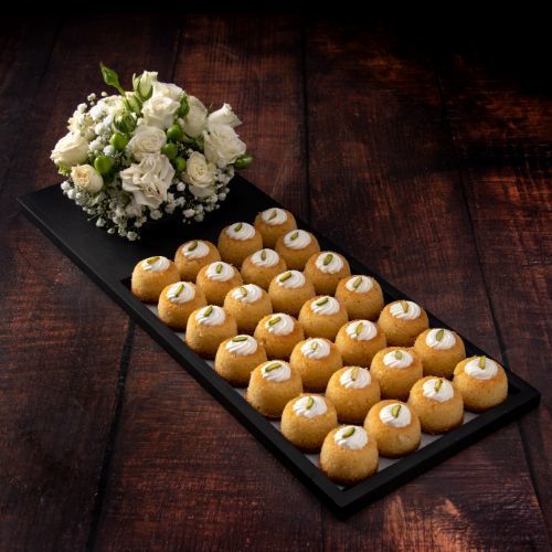 Mini Basbousa with Fresh Cream - 24 pieces of mini basbousa with cream, perfect for gatherings, served on a wooden tray designed with fresh flowers.