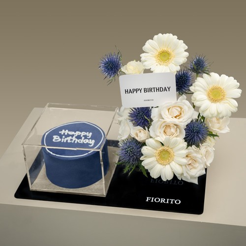 Vibrant Wishes - An acrylic tray topped with baby roses, gerberas, and eryngium with a cake. Adds a touch of elegance and draws smiles on their birthdays. Note: cake writing is customizable.