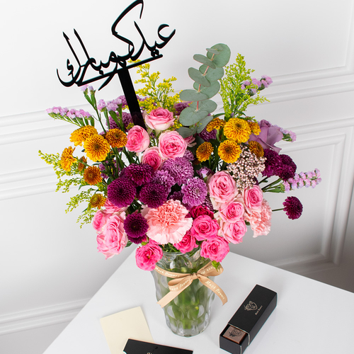 Bazaar - A vase filled with roses, carnations, and chrysanthemums arranged beautifully with chocolates, and an acrylic topper.