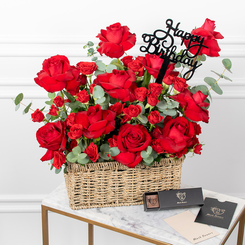Flowers Day - Red roses arranged beautifully in a basket with chocolates, a card, and an acrylic topper.