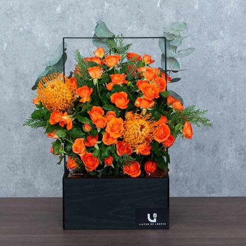 Orange Poppy - A black wooden basket with metal handle contains baby roses, leucospermum and eucalyptus with Belgian chocolates.  Height: 50cm – Width: 45cm