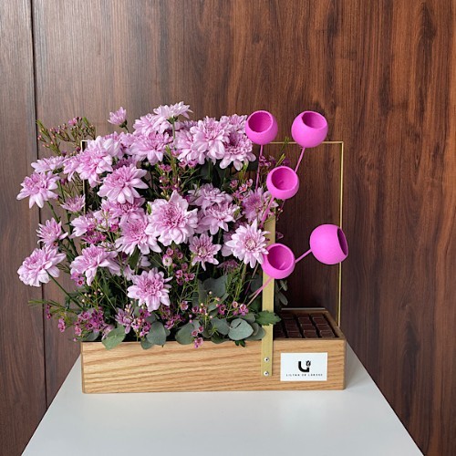 Pastel Pink - This wooden basket contains pink chrysanthemum, wax flower, stick bell and Eucalyptus with Belgian chocolates.  Height: 53cm – Width: 55cm