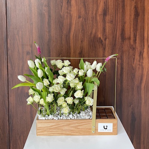 ساندي - هذه السلة الخشبية تحتوي على زهور البيبي جوري البيضاء والتوليب الأبيض مع الشوكولاتة البلجيكية.  الطول: 51 سم العرض: 54 سم