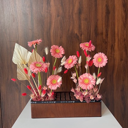 Trendy Edit - This wooden rectangle contains gerbera, palm leaves and triticum with Belgian chocolates.  Height: 45cm – Width: 50cm