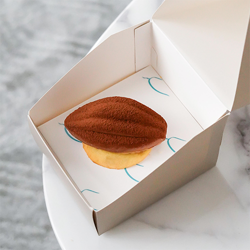 Cocoa Praline Gem - A cake shaped like a cocoa pod, with layers of chocolate and hazelnut praline cream, filled with cream and a touch of caramel, coated in chocolate and dusted with cocoa.Ask ChatGPT