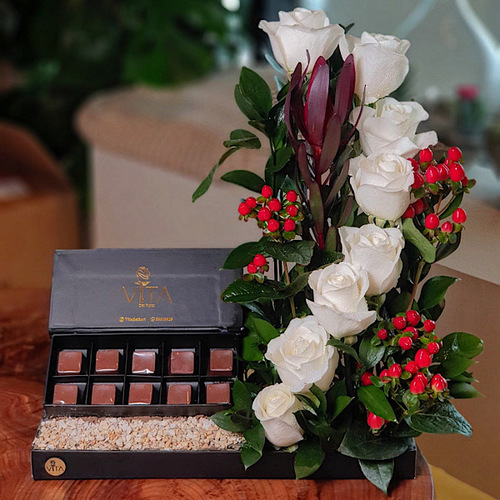 Optical - This black tray contains white roses and red hypericum flowers with green leaves. Comes with a box of chocolates. H : 55 W : 30