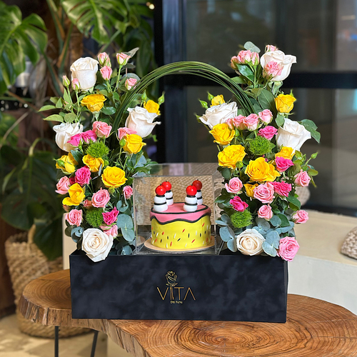 Tej - A black box that contains pink, yellow baby roses, white roses green leaves with a cake. Height: 55 Width: 40