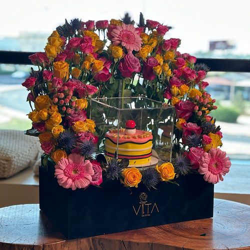 Stefany - Black box contains deep purple yellow & pink roses and baby roses pink, yellow Hypericum pink, Gerbera pink Eryngium and eucalyptus with a cake.  Height: 50 Width: 40