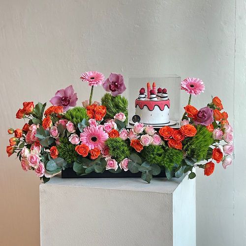 Perfection - A tray elegantly filled with pink and orange baby roses, purple cymbidium, gerbera and green leaves with a cake. Height: 40 Width: 25