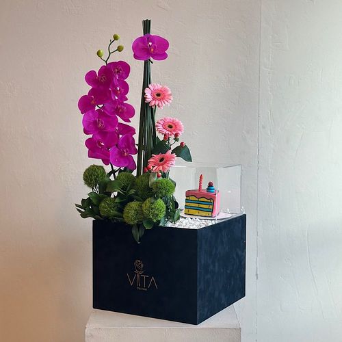 Olympic - A box filled with purple orchid cut flowers, steel grass, gerbera, hypericum and green leaves with a cake. Height: 70 Width: 40