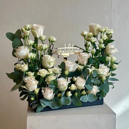 Kofler - A tray that contains white Roses, baby rose white, eucalyptus with a congrats gold stick. Height: 50 Width: 20
