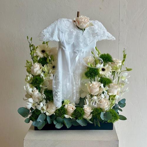 Cluj - A tray that contains white roses, gerberas, and baby orchids with dianthus and eucalyptus leaves. Comes with a white dress for a newborn baby. Height: 60 Width: 20