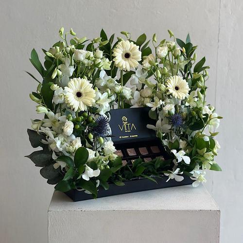 Hiom - Tray elegantly filled with white grabera, green leaves, white baby orchid hypericum green,eryngium,  with a box of chocolates.. Height: 50 Width: 30