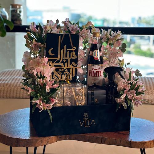 Belasima - A black box that contains pink baby orchid, green leaves with a spray perfume, a box of chocolates, a box of mixed dates (sesame, coconut, nuts) and a Vimto bottle. Height: 60 Width: 40