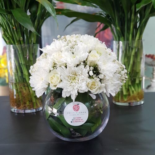 The White - White Craze And White Baby Rose In Medium  Round Glass Vase 519 - Baby Rose White, White Craze, Gypsophilia And Green Ruscus In Round Glass Vase.  Height- 20 cm Width- 20 cm